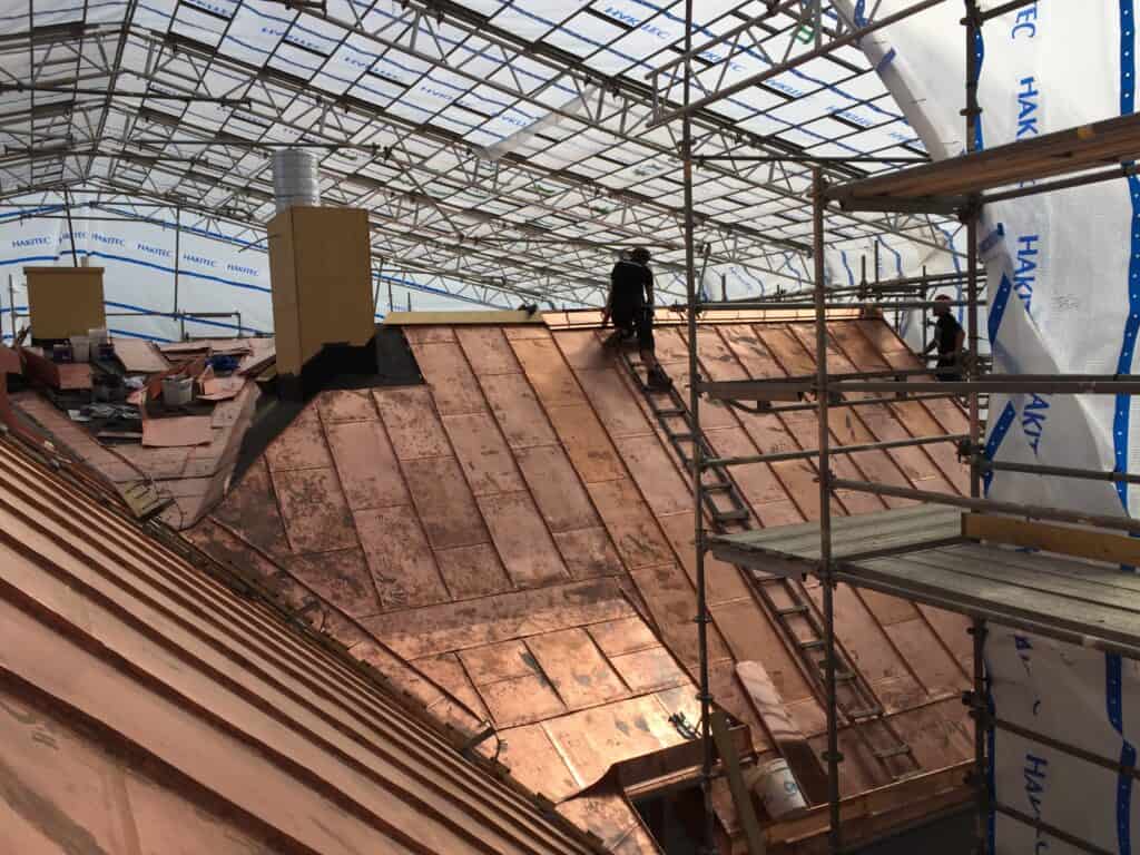 Hantverkare arbetar med koppartak på byggarbetsplats – takrenovering i G.F. Consultings regi